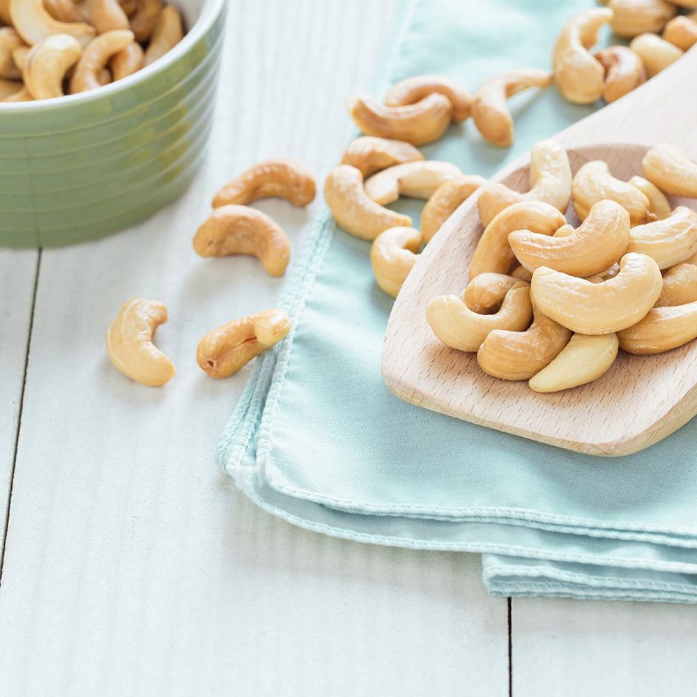 Anacardi su un cucchiaio di legno e su un panno blu. Ciotola verde sullo sfondo.
