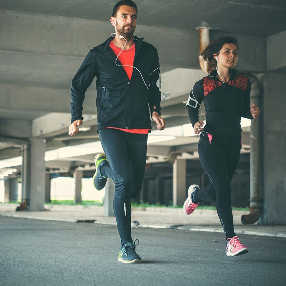 Due corridori, uomo e donna, in abbigliamento sportivo. Corrono su una strada sotto un ponte. Attività sportiva.
