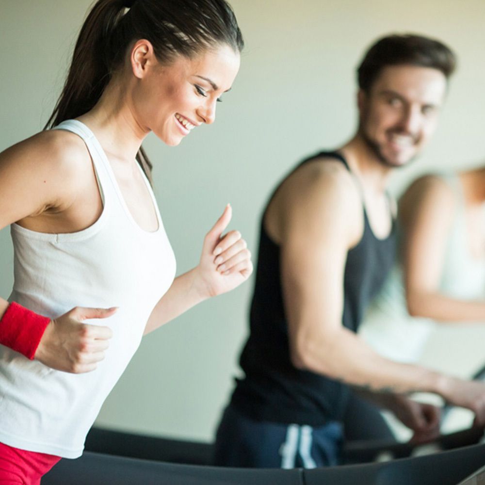 Donna e uomo su tapis roulant in palestra. La donna sorride. Attività sportiva.