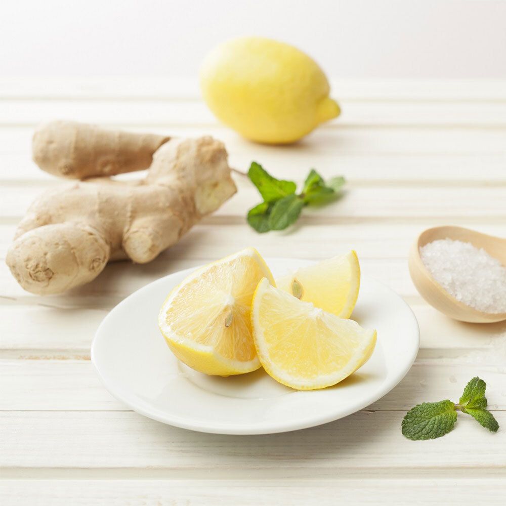 Fette di limone su un piatto, zenzero, menta e sale accanto. Su sfondo di legno chiaro.