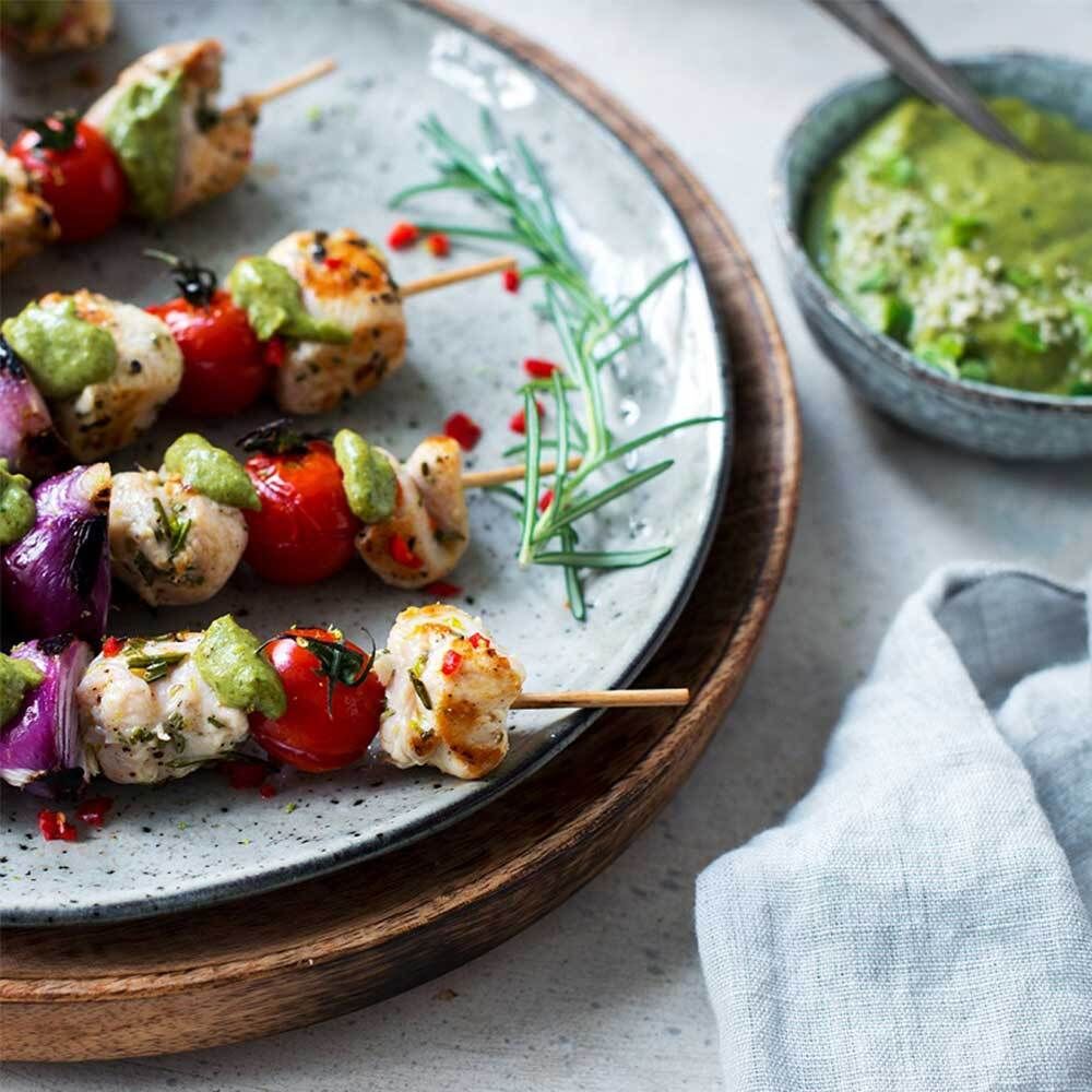 Piatto con spiedini di pomodori, pollo e cipolle. Con salsa verde e rametto di rosmarino.