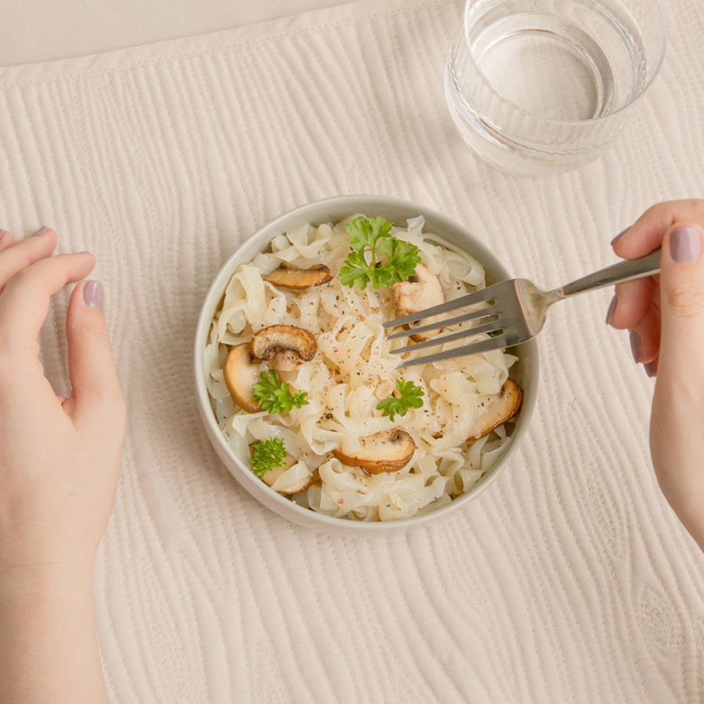 Una ciotola di konjak-tagliatelle con funghi e prezzemolo, fotografata dall'alto, con una forchetta.