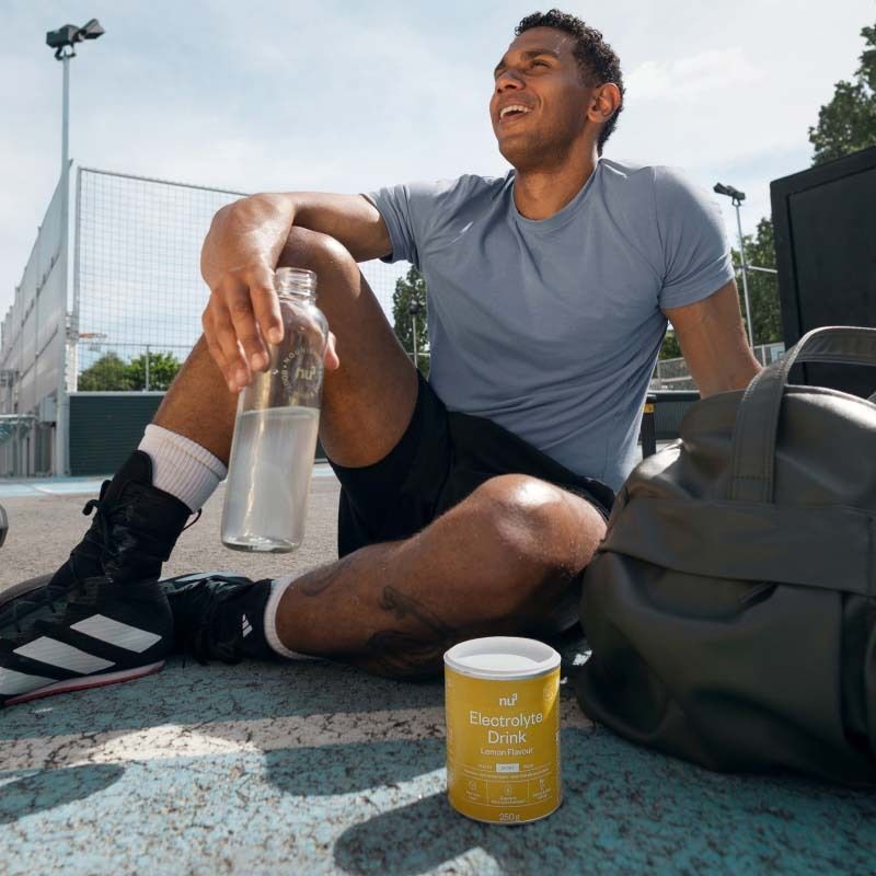 Uomo seduto dopo lo sport accanto alla lattina Nu3 Elektrolyte Drink e una bottiglia d'acqua.