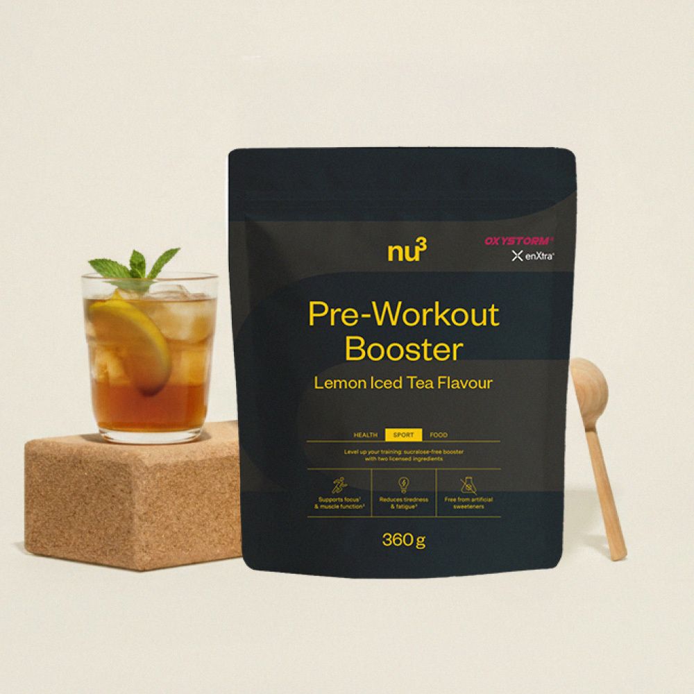 Confezione nera "nu3 Pre-Workout Booster" accanto a bicchiere, cucchiaio legno. Gusto tè freddo al limone.