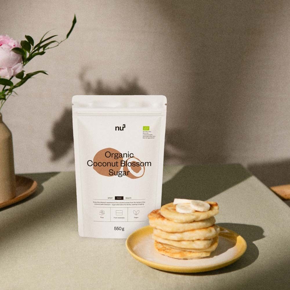 Confezione prodotto accanto a pancake su piatto giallo. Fiori in vaso. Scritta "Organic Coconut Blossom Sugar".