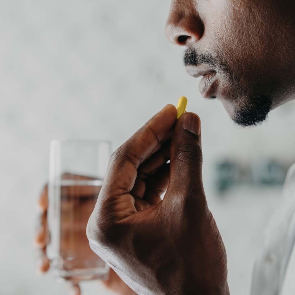 Persona che prende una capsula gialla. Un bicchiere d'acqua è visibile. L'uomo ha la barba.