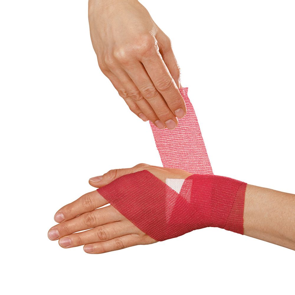 Mani che avvolgono una benda di fissaggio Peha-haft rossa attorno al polso e alla mano. Benda rossa.