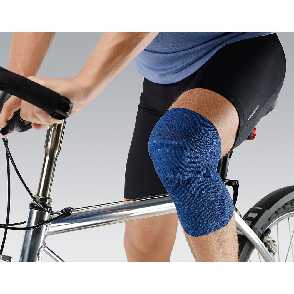 Persona in bicicletta con benda Peha-haft® Color blu sul ginocchio. La benda copre il ginocchio.