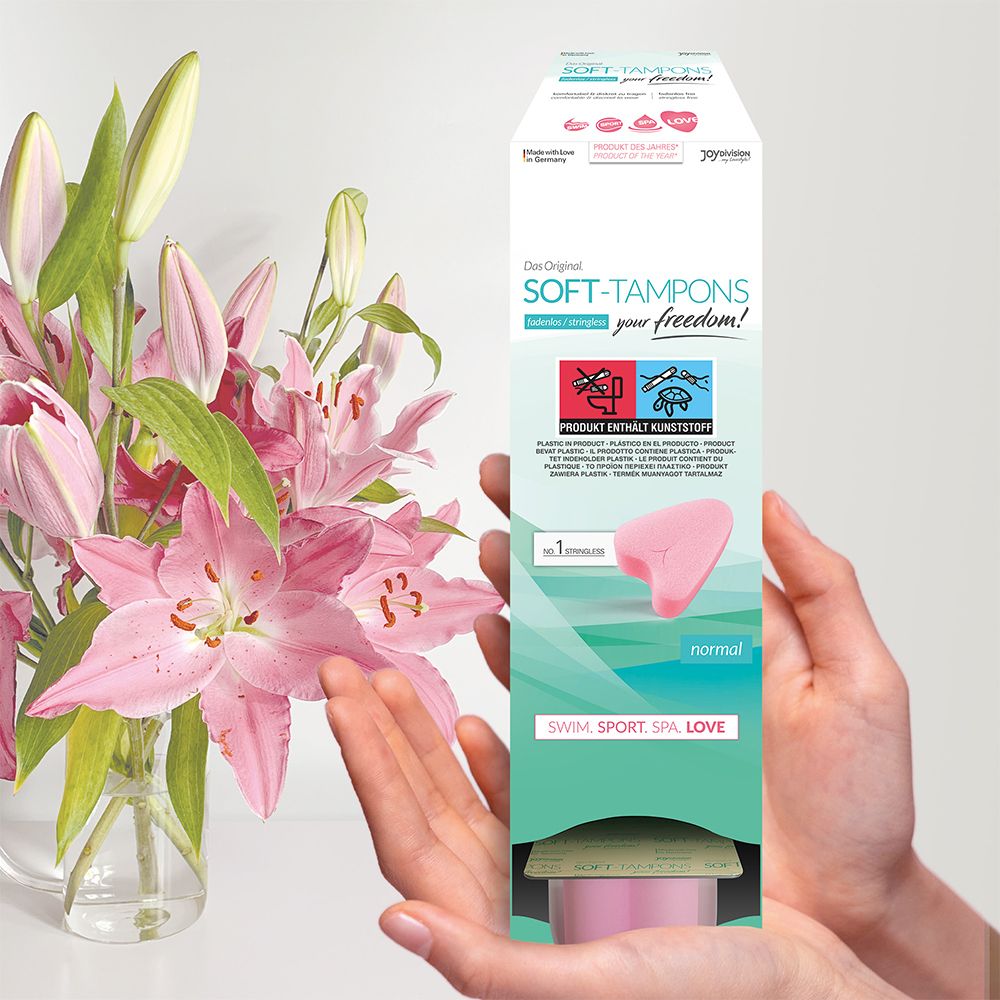 Persona che tiene in mano una confezione di tamponi morbidi rosa. Testo: Das Original SOFT-TAMPONS, normal. Per nuoto, sport, spa, amore.