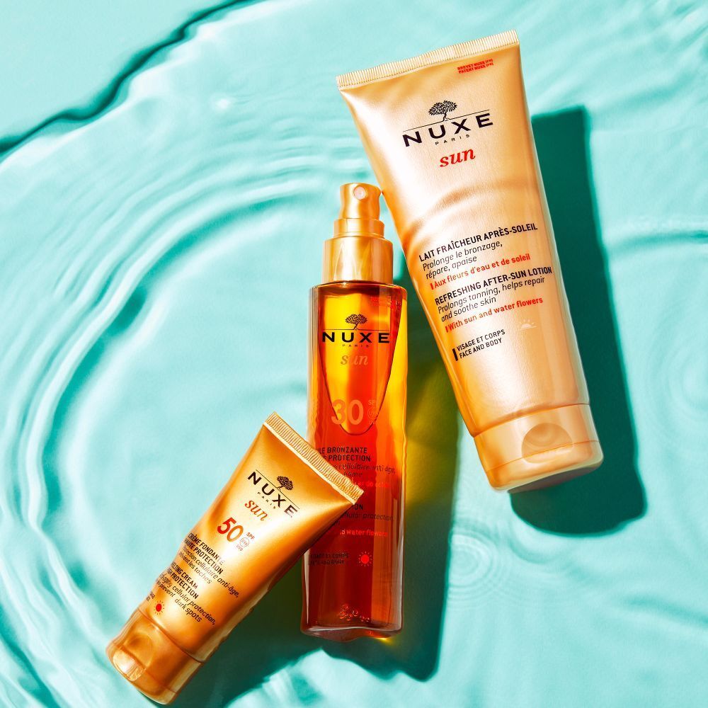 Prodotti NUXE Sun: crema solare, lozione doposole, olio solare. Testo: Lait Fraîcheur, Huile Bronzante. Su acqua blu.