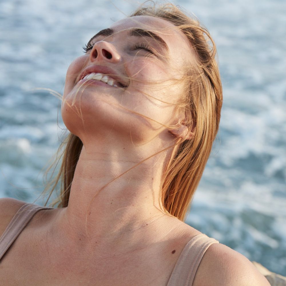Donna con gli occhi chiusi, sguardo verso l'alto. Pelle al sole. Capelli al vento.