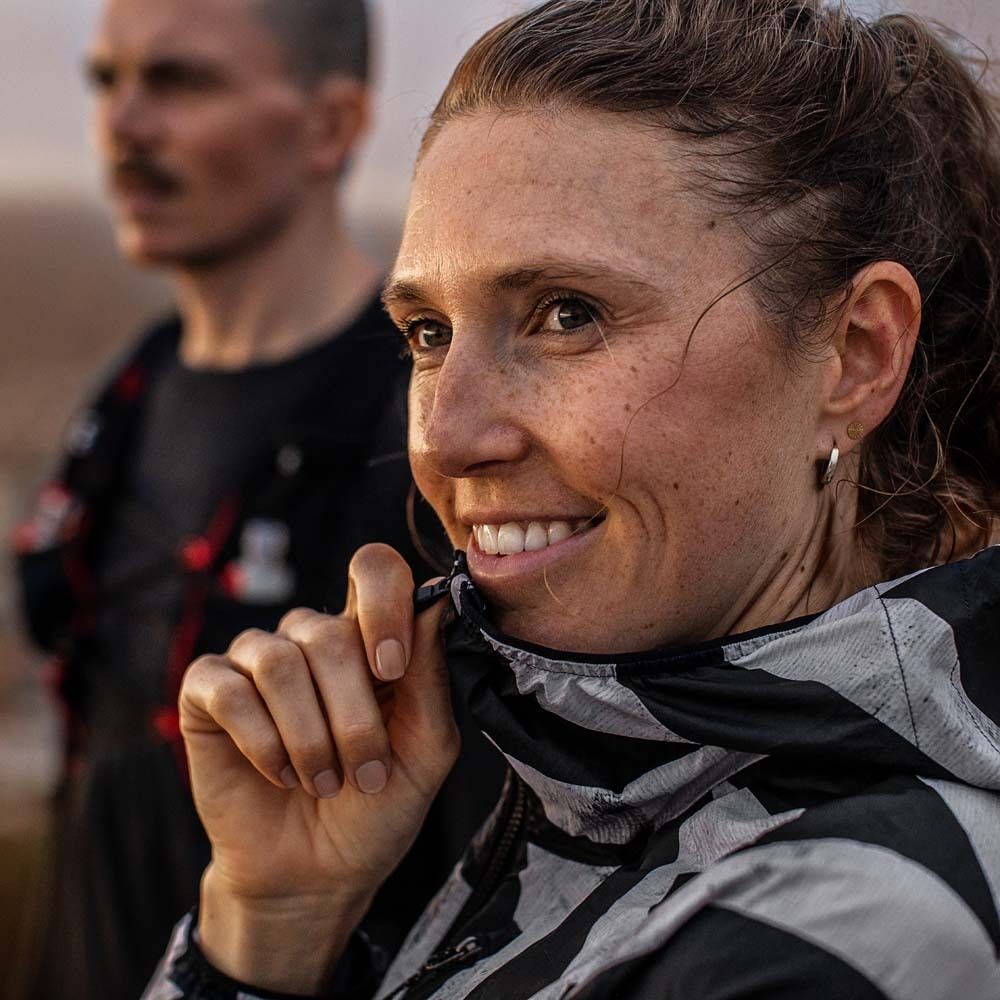 Ritratto di una donna sorridente con una giacca a righe bianche e nere. Un'altra persona sullo sfondo.