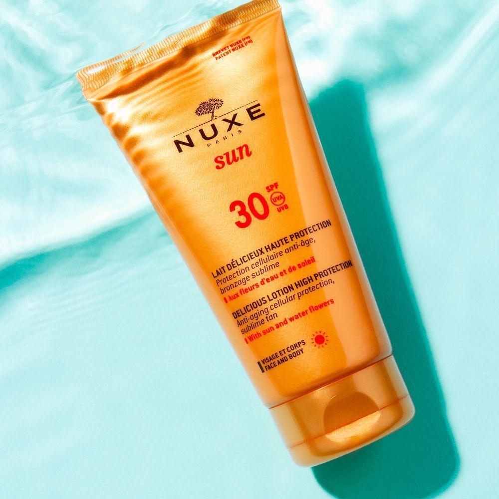 Tubo di latte solare dorato. NUXE Sun, SPF 30. Su sfondo blu. Testo: Lait Délicieux Haute Protection.