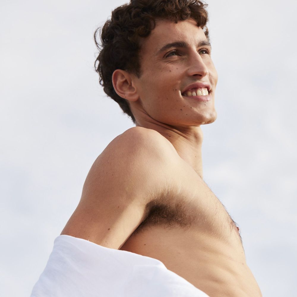 Uomo, a torso nudo, sorridente. Guarda in alto. Luce solare intensa.