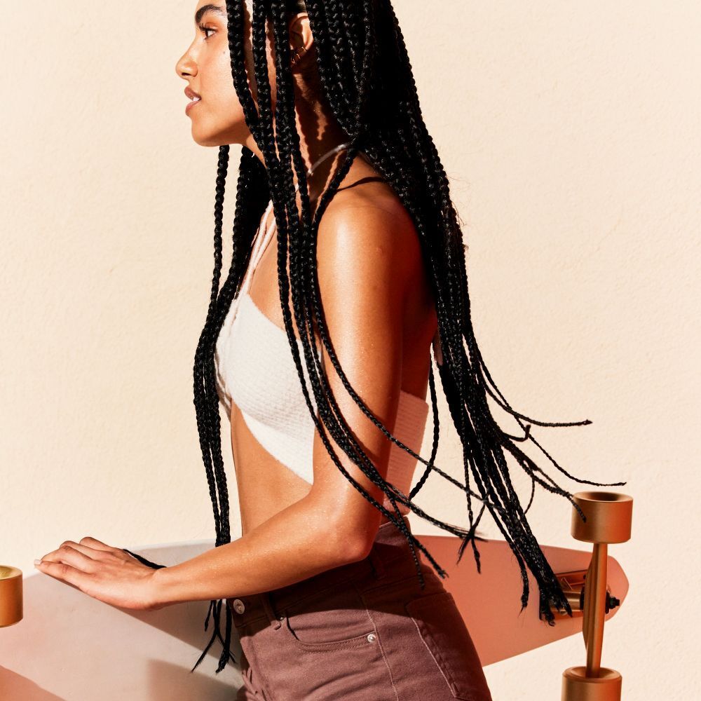 Donna con trecce e skateboard. Pelle abbronzata. Pelle con lucentezza.