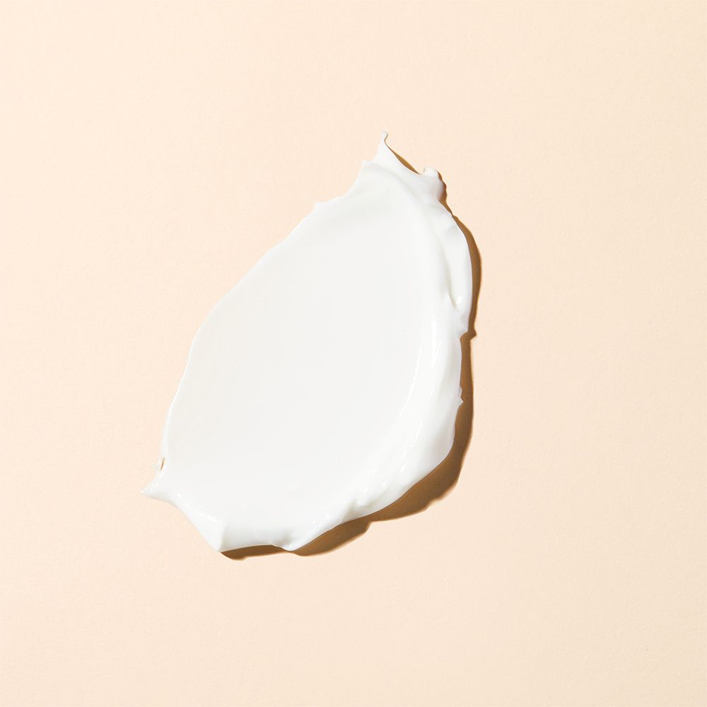 Macchia di crema su sfondo beige. Colore bianco, consistenza liscia.