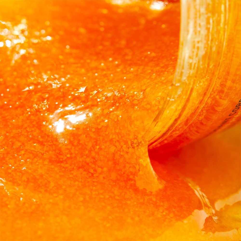 Primo piano dello scrub che esce da un barattolo. Texture granulosa arancione.