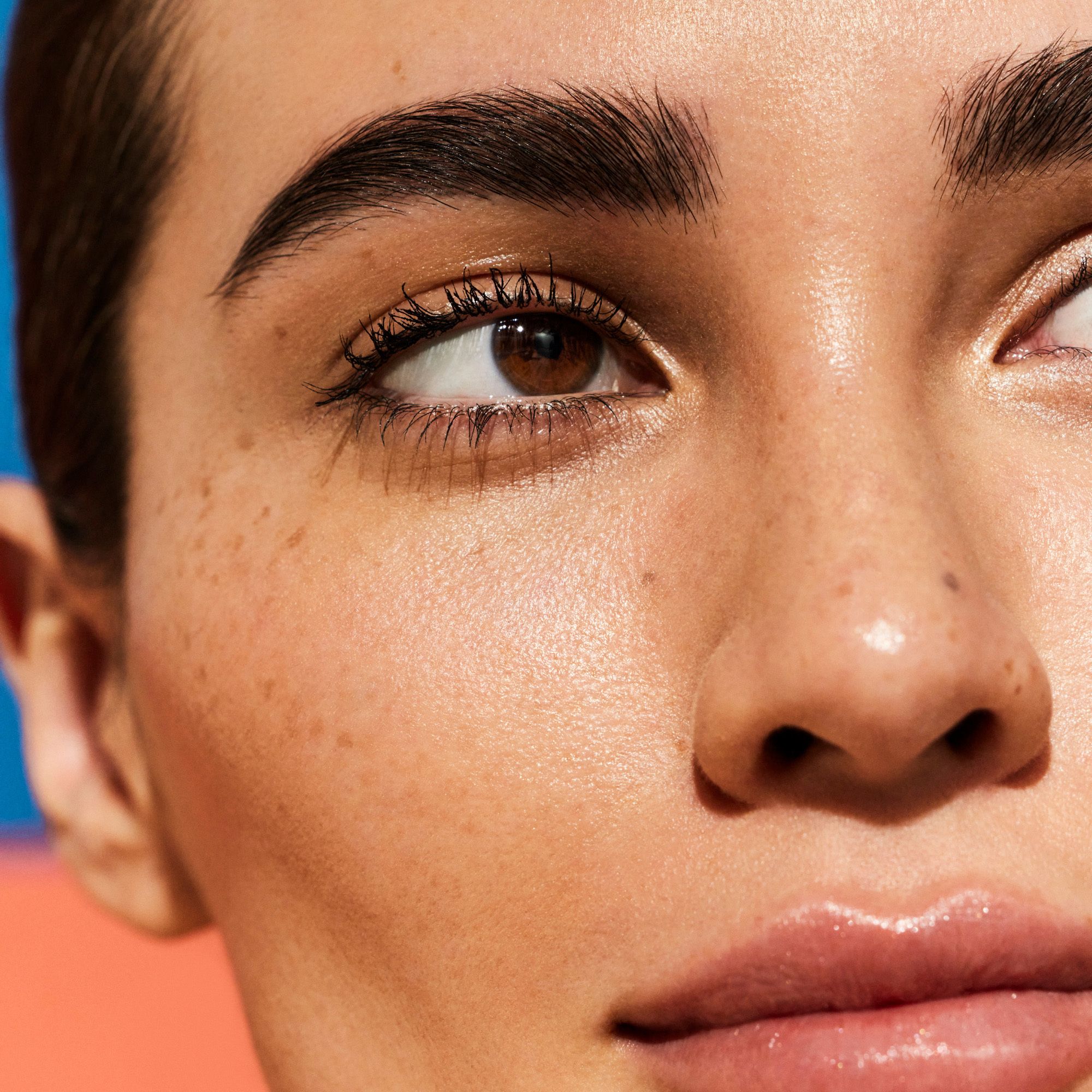 Primo piano di un viso. La pelle brilla. Occhi marroni, sopracciglia scure, labbra chiare.