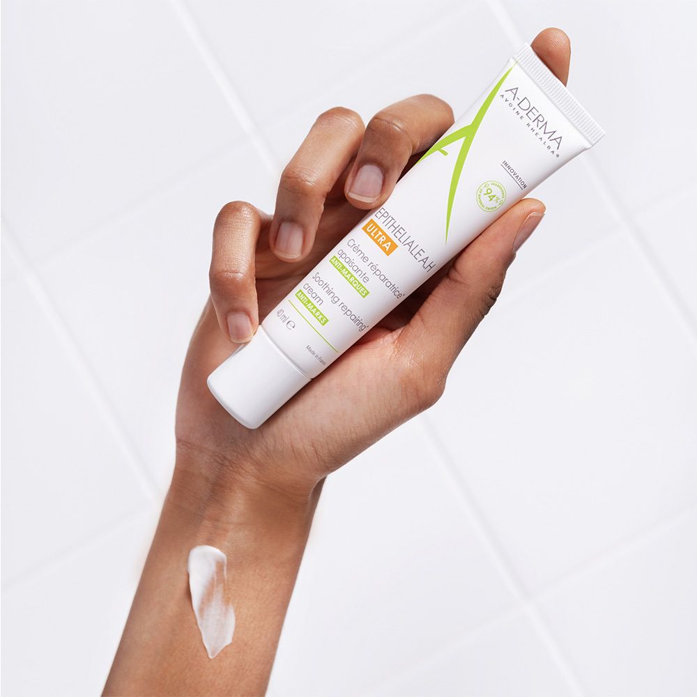 Mano che tiene un tubo A-DERMA EPITHELIALE A.H ULTRA. Crema applicata sul braccio. Bianco, 40 ml.