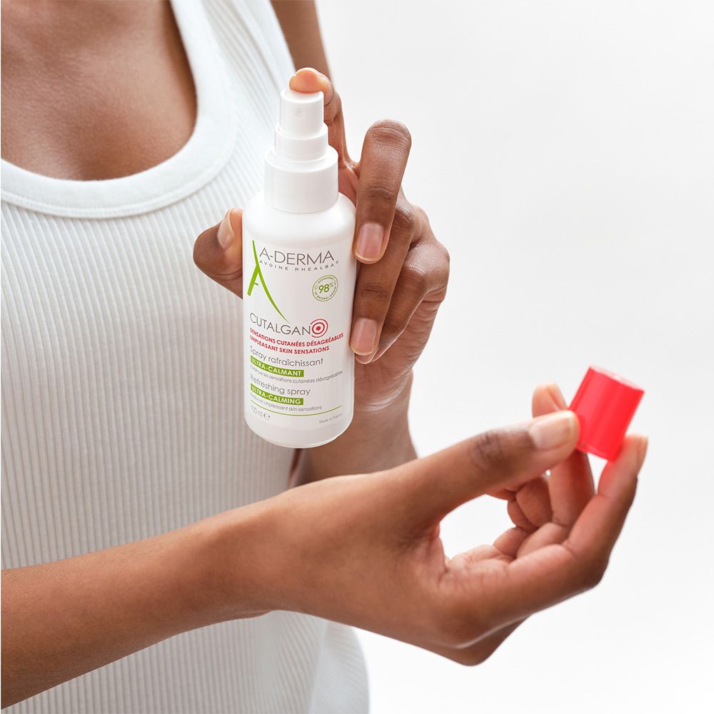 Persona che tiene A-DERMA Cutalgan Spray. Tappo rosso in mano.