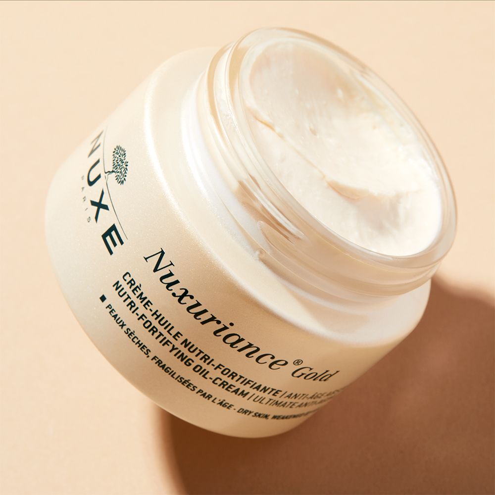 Vasetto di crema aperto con coperchio dorato. Scritta: Nuxuriance Gold, Crème-Huile Nutri-Fortifiante.