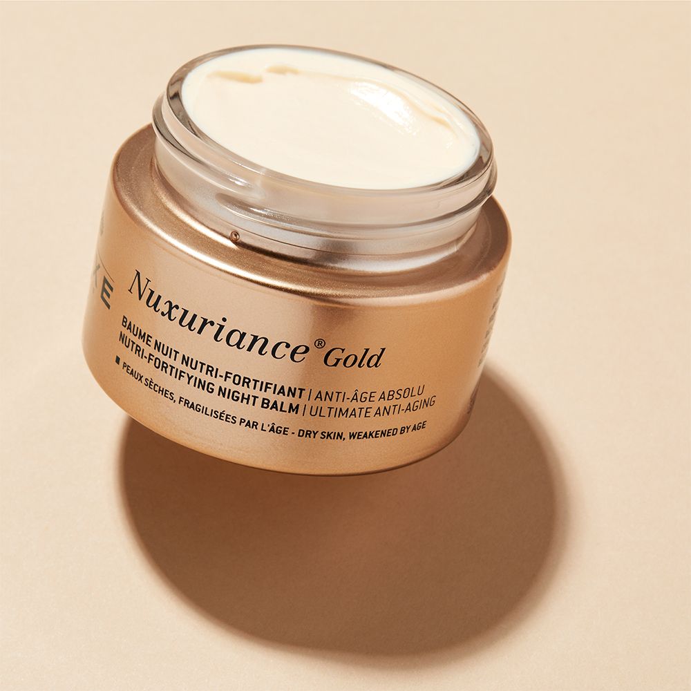 Vasetto dorato aperto. Scritta: Nuxuriance Gold. Crema visibile.