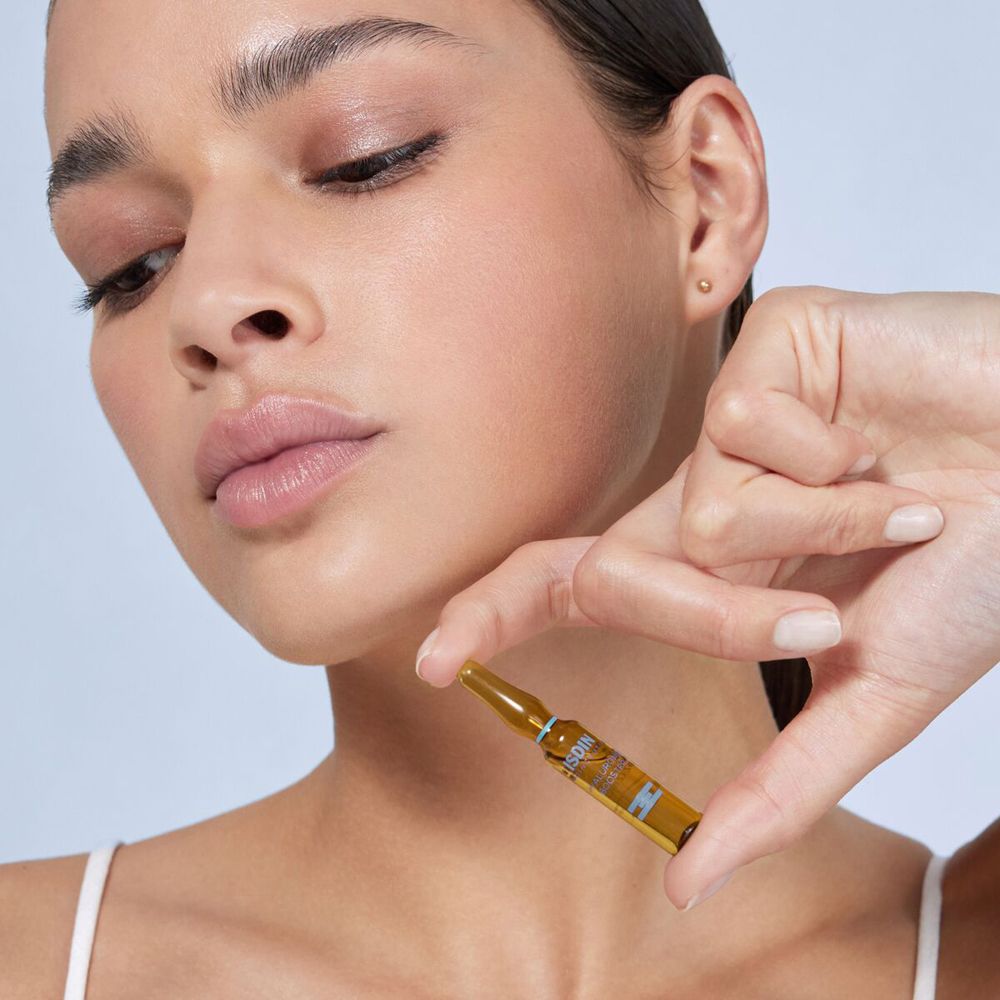 Donna tiene in mano una fiala di ISDINCEUTICS Hyaluronic Booster. Prodotto visibile. Primo piano.