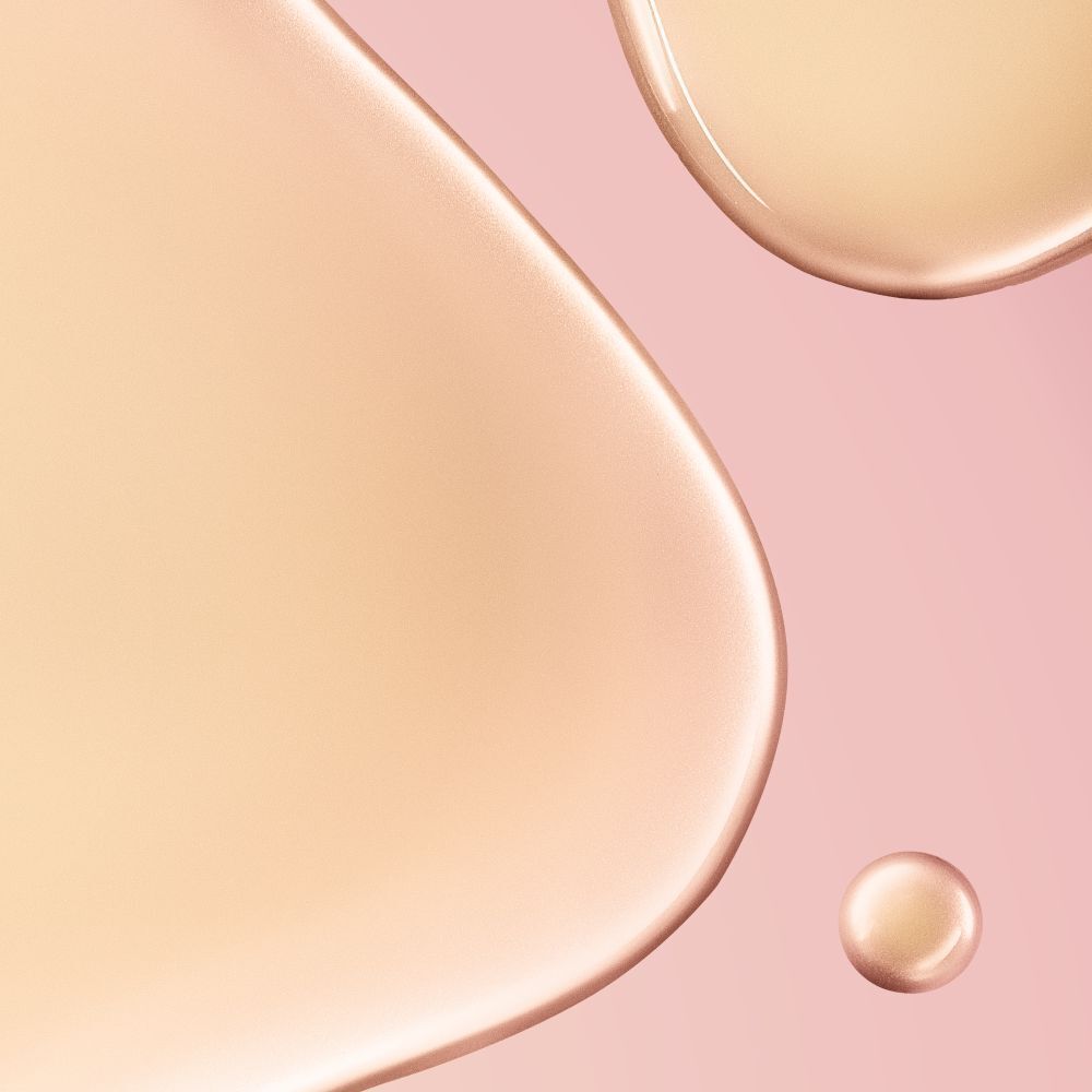 Primo piano di gocce di liquido giallastro su sfondo rosa. Una piccola goccia sotto.