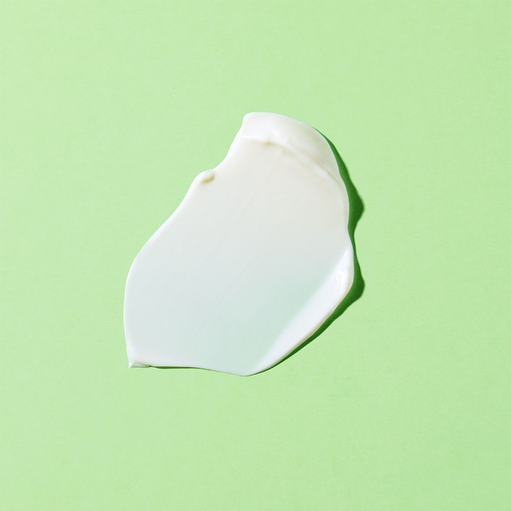 Macchia di lozione per il corpo su sfondo verde. Crema bianca.