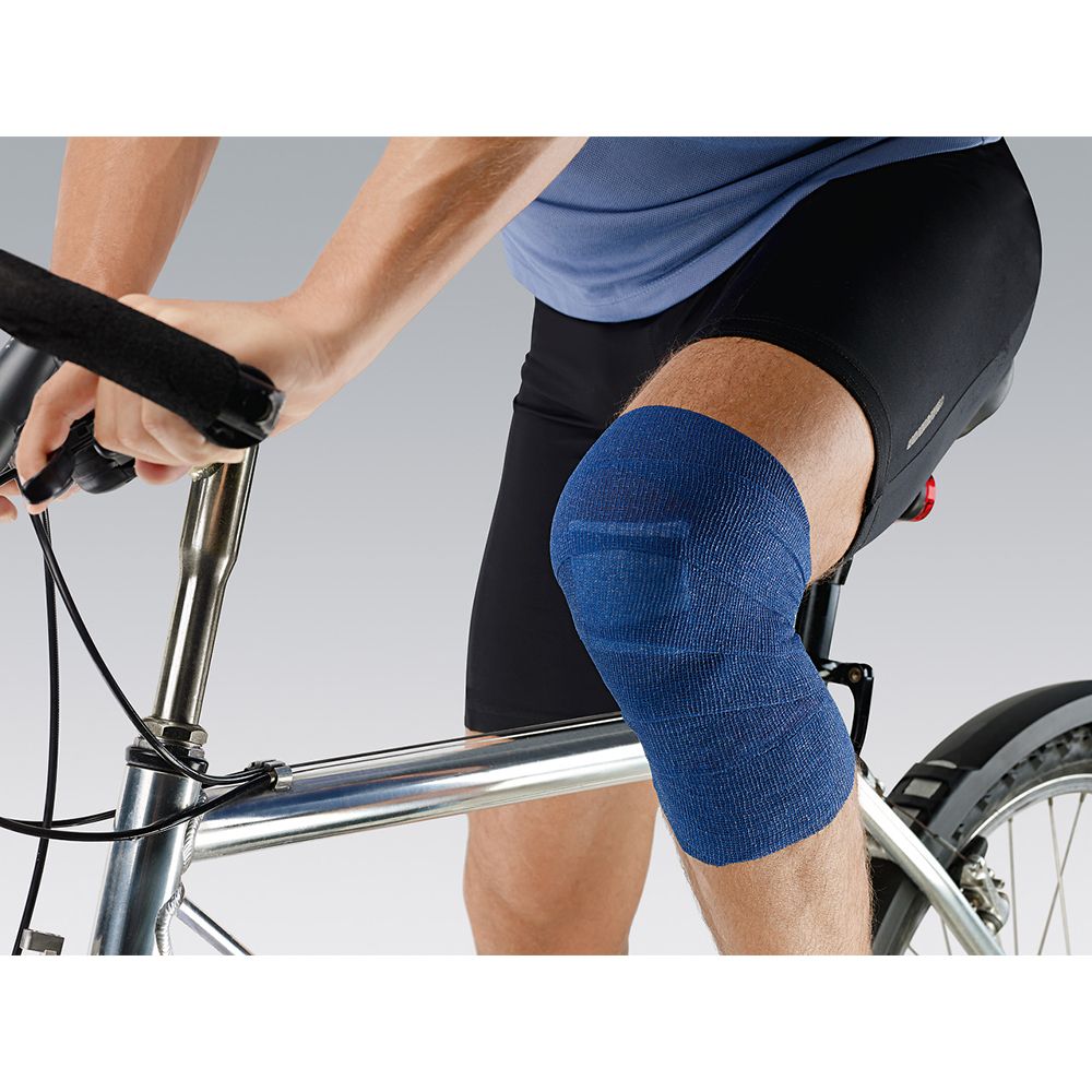 Ginocchio di un ciclista con bendaggio blu Peha-haft® Color. Il bendaggio copre il ginocchio.