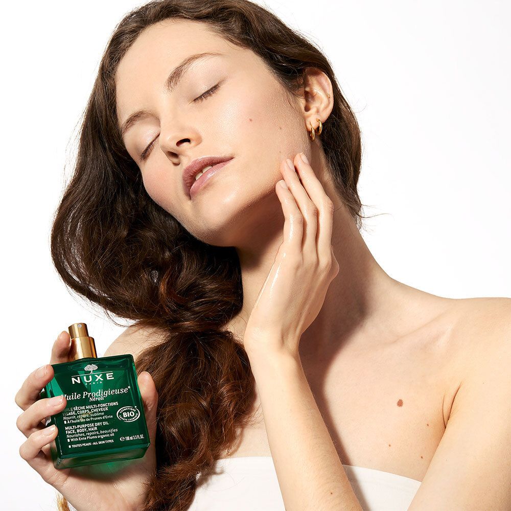 Donna con capelli lunghi che tiene in mano un flacone verde con tappo dorato. Viso.