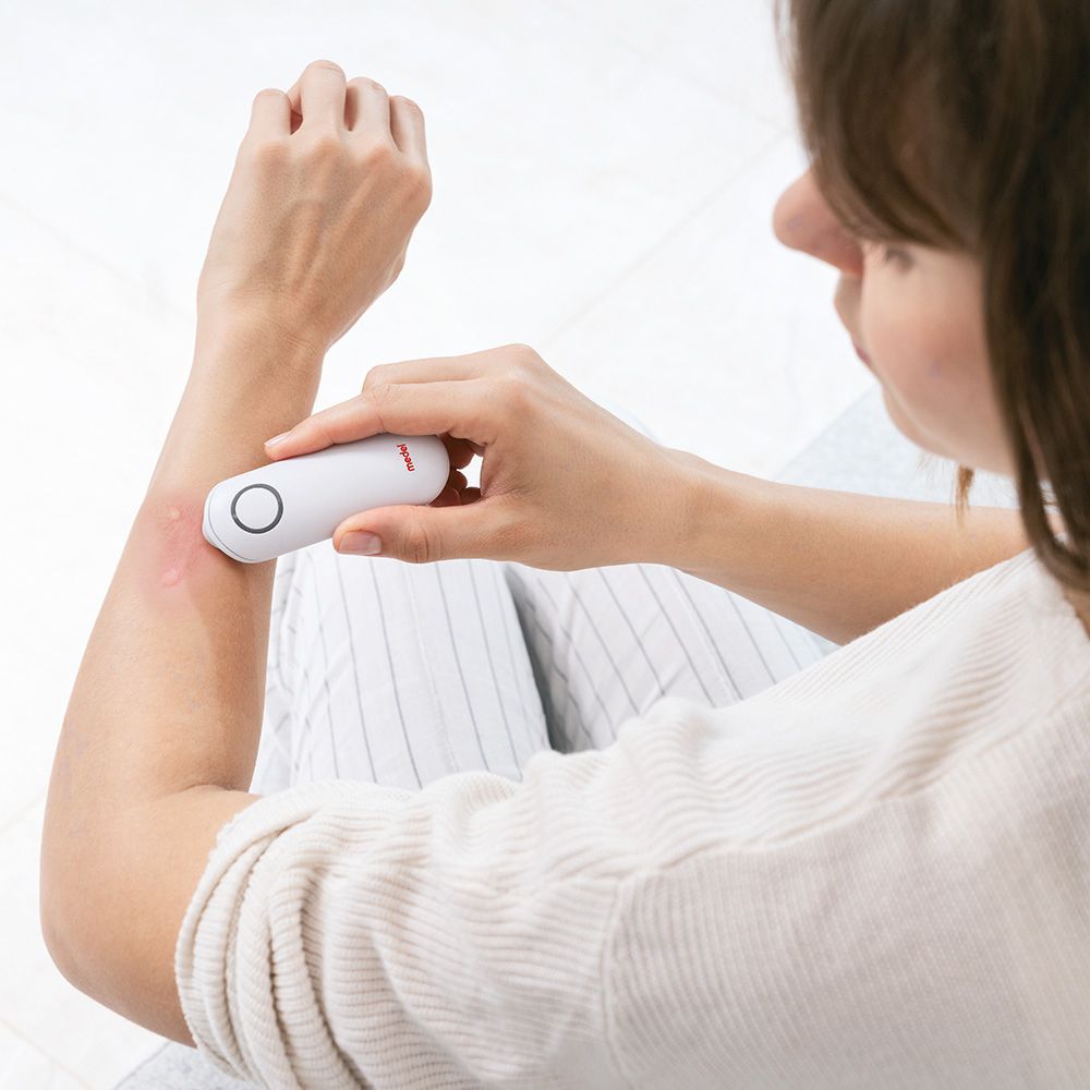 Persona tiene dispositivo bianco sul braccio. Puntura rossa visibile. Nome "medel" sul dispositivo.