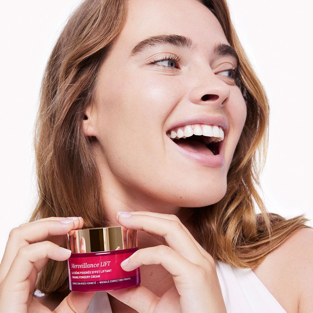 Donna che tiene un vaso di crema. Scritta: Merveillance LIFT, NUXE PARIS. Vaso rosso con coperchio dorato.