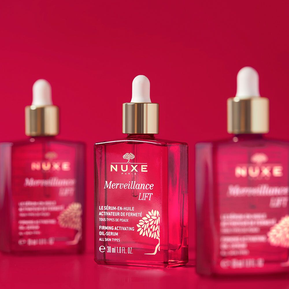 Tre flaconi di vetro rosso con tappi dorati. Scritta: NUXE Merveillance Lift, siero olio, tutti i tipi di pelle.