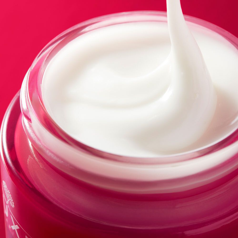Primo piano di crema bianca che esce da un vasetto rosso. Sfondo rosso.