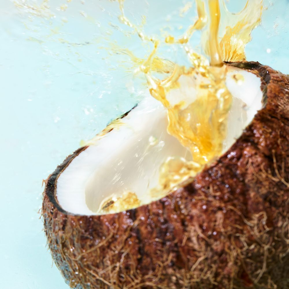 Mezza noce di cocco con spruzzi di liquido. Sfondo azzurro.