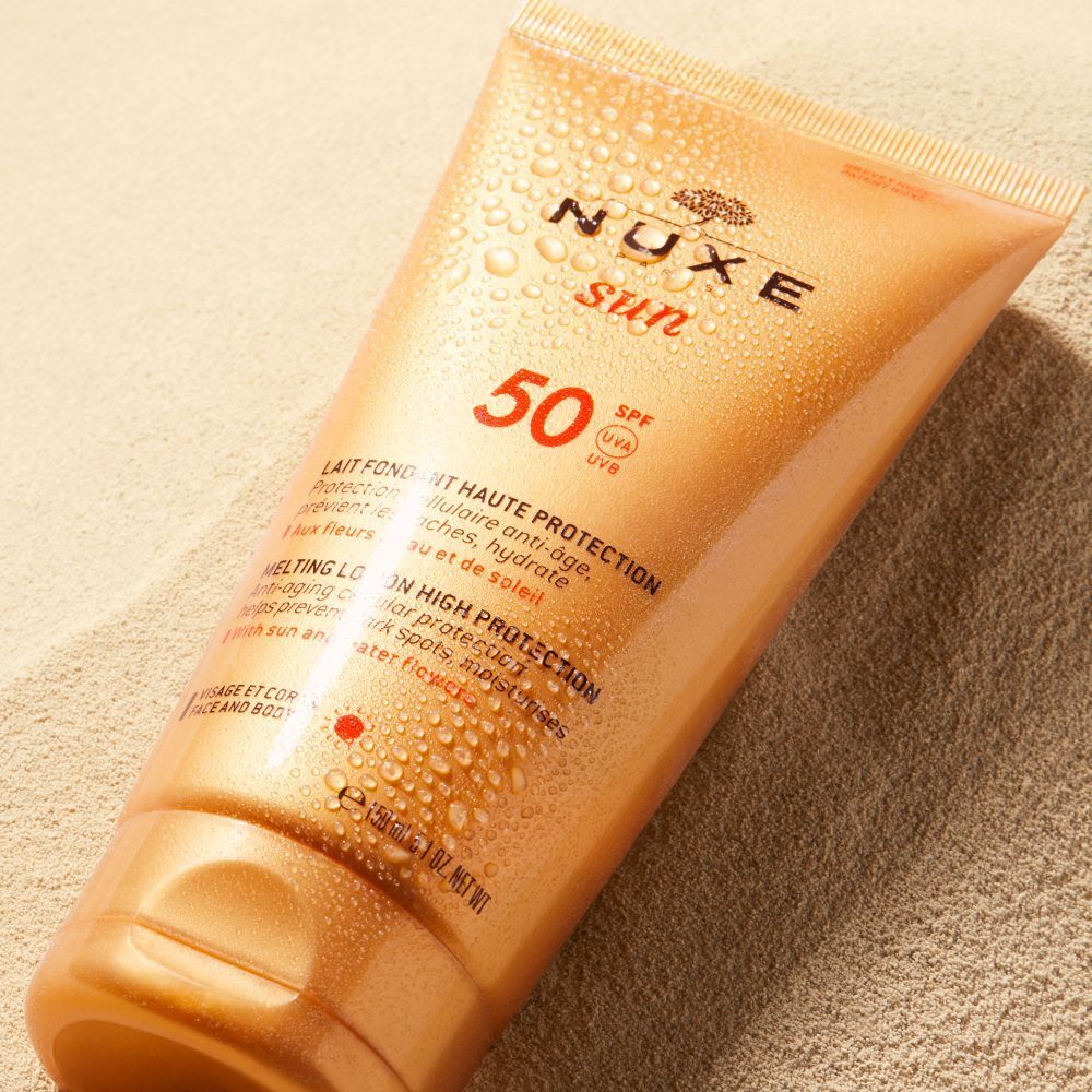 Tubo di crema solare NUXE Sun, SPF 50, sulla sabbia. Gocce d'acqua sul tubo.