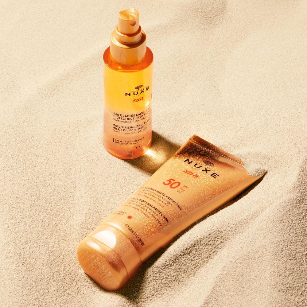 Due prodotti NUXE Sun sulla sabbia. Tubo di crema solare e flacone spray.