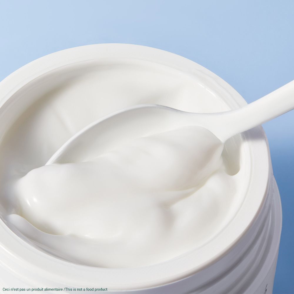 Prodotto in crema bianca in un vasetto. Un cucchiaio si immerge nella crema. Sfondo azzurro.