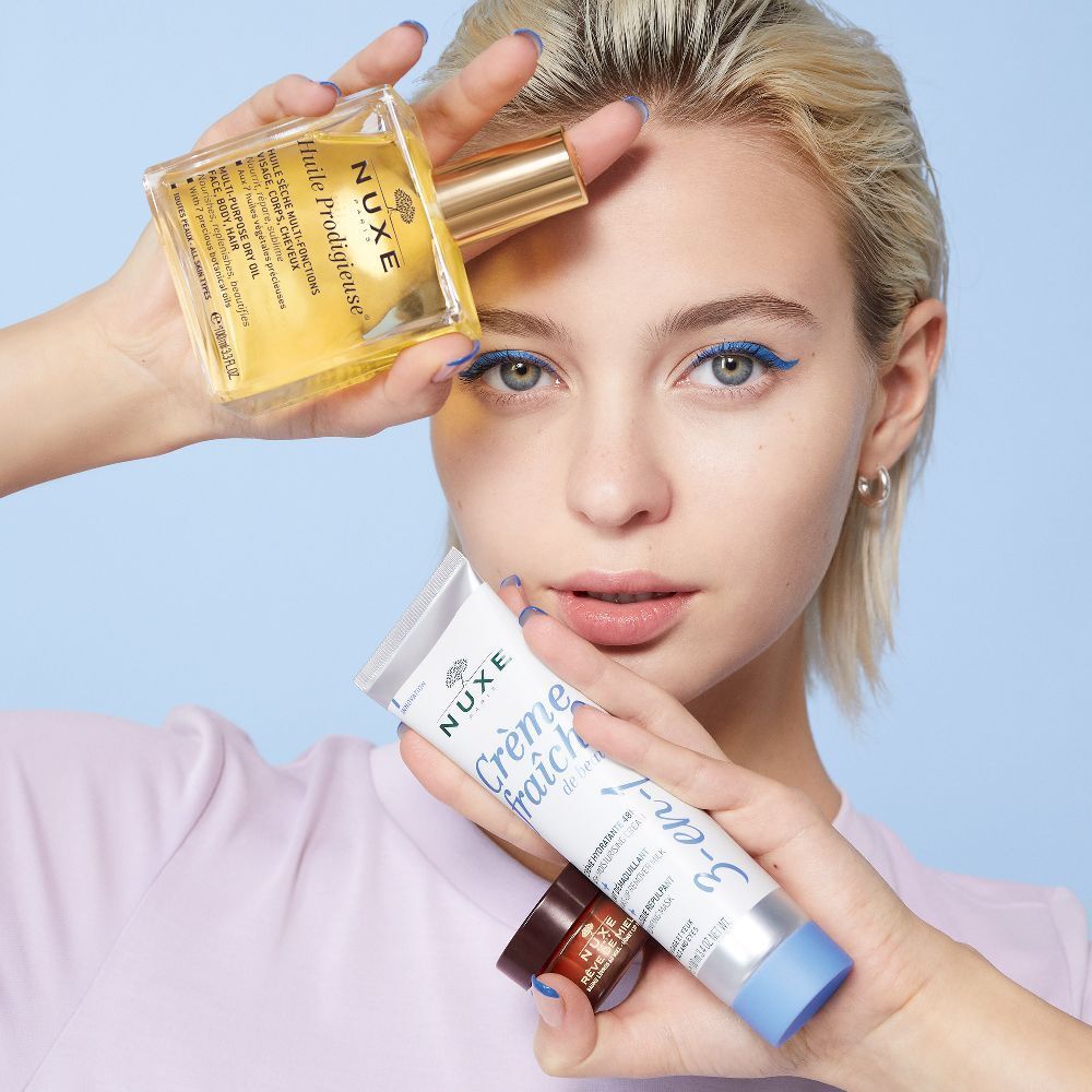 Donna con prodotti. Prodotti: vasetto di crema, tubo, olio, balsamo labbra. Scritta: Crème fraîche de beauté. Sfondo azzurro.