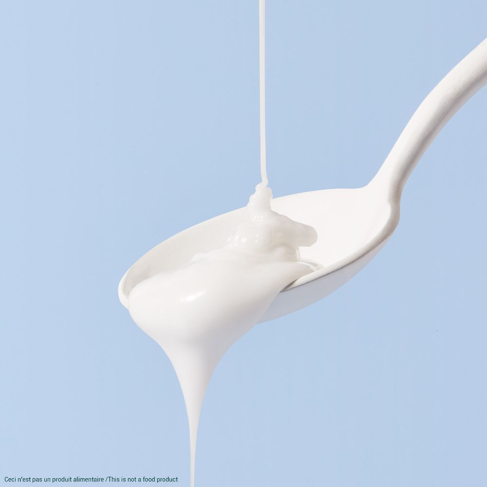 Prodotto bianco che cola da un cucchiaio. Sfondo blu.