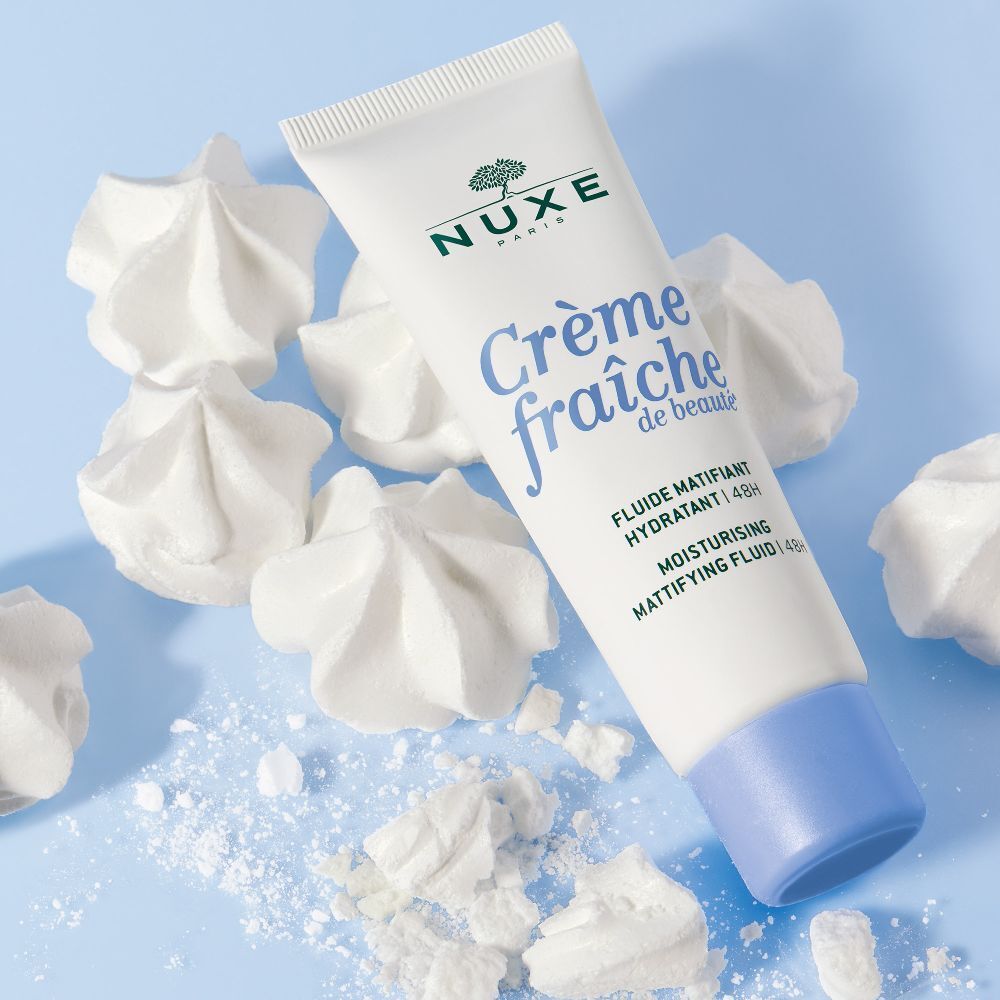 Tubo bianco con tappo blu, circondato da meringhe bianche. Scritta: NUXE, Crème fraîche de beauté.