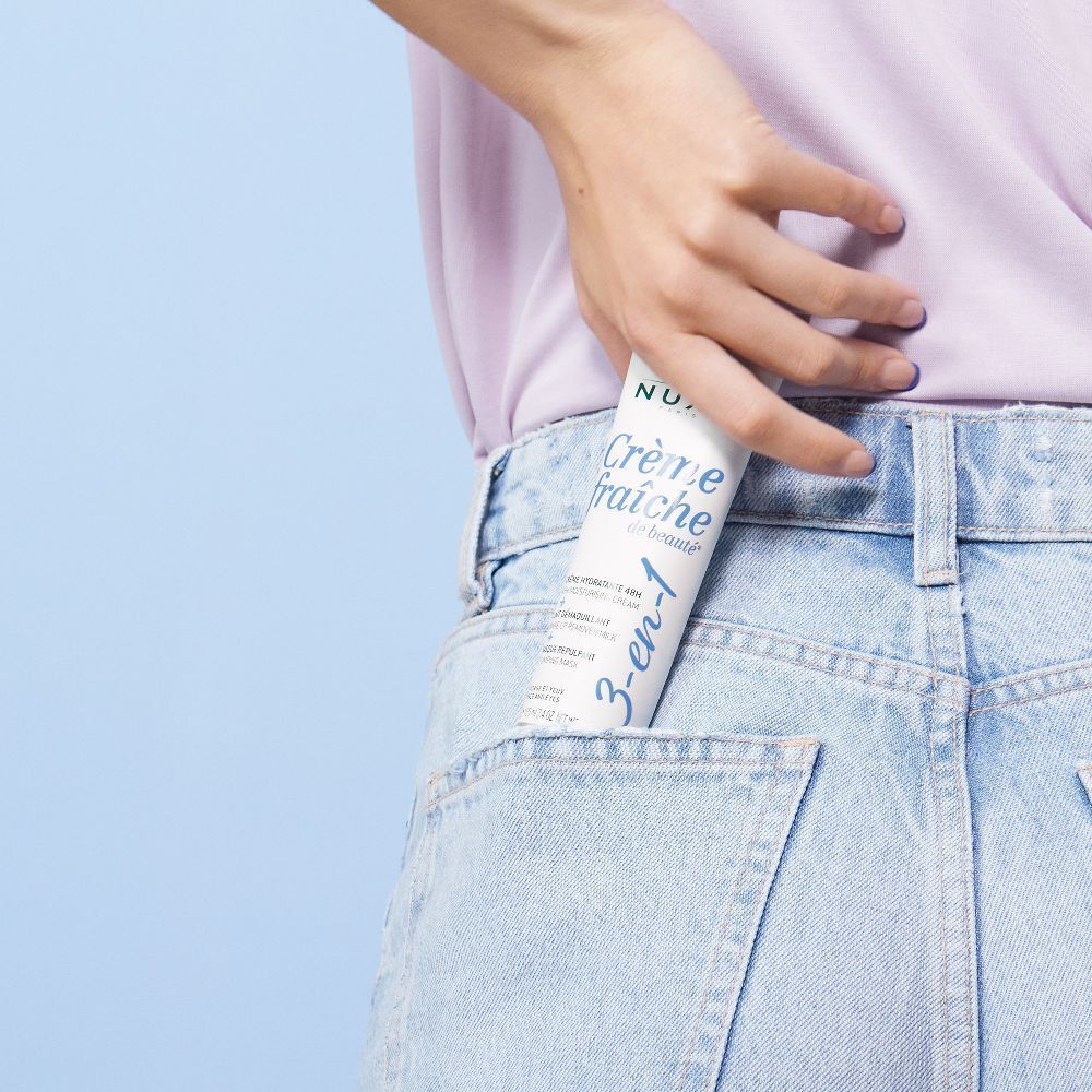 Tubo di Crème Fraîche de Beauté in tasca dei jeans. Bianco, blu e argento. Testo: Nuxe, Crème Fraîche de Beauté, 3-en-1.