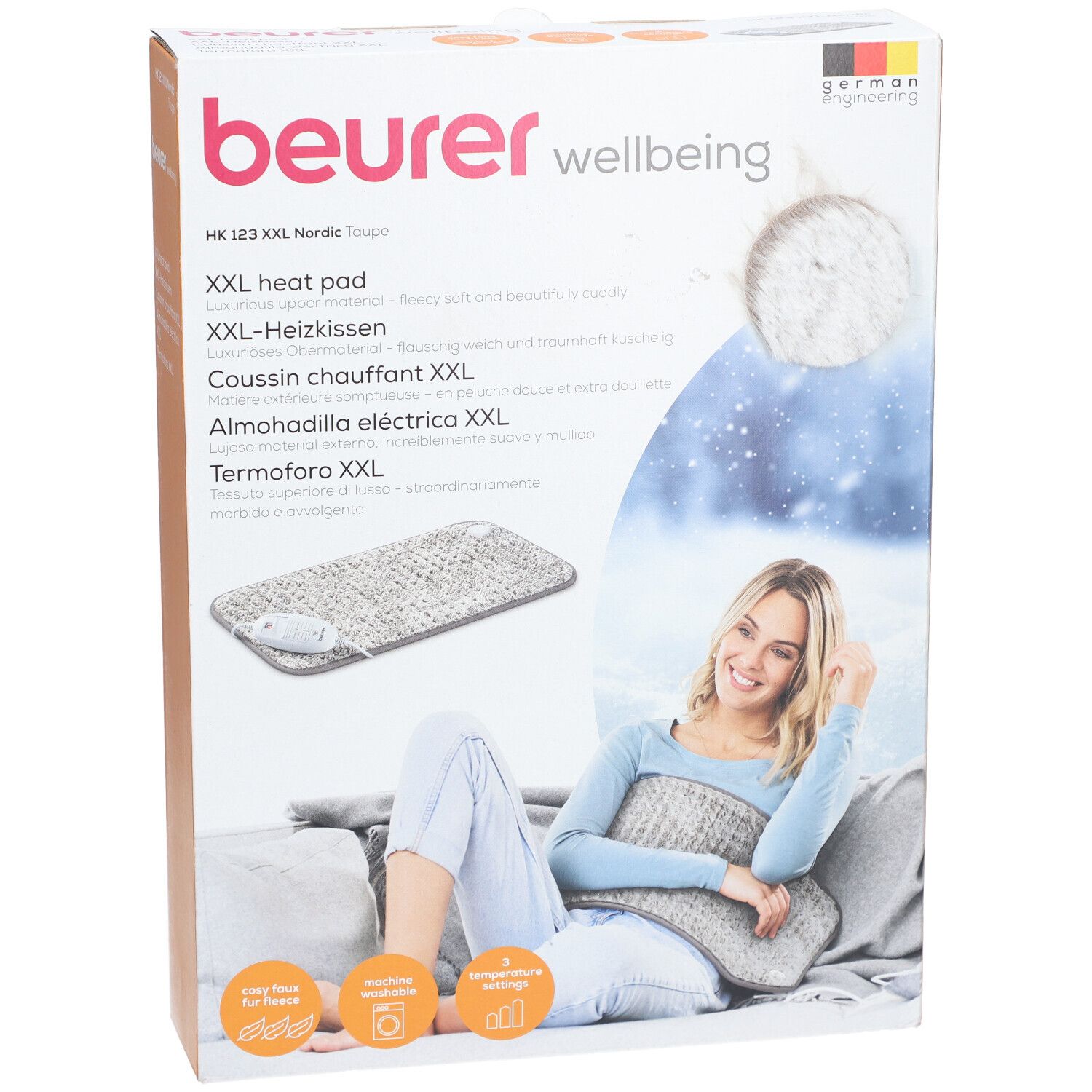 Confezione del prodotto. Cuscino riscaldante Beurer HK 123 XXL Nordic. Immagine: cuscino riscaldante, donna con cuscino. Testo: cuscino riscaldante XXL, German Engineering.
