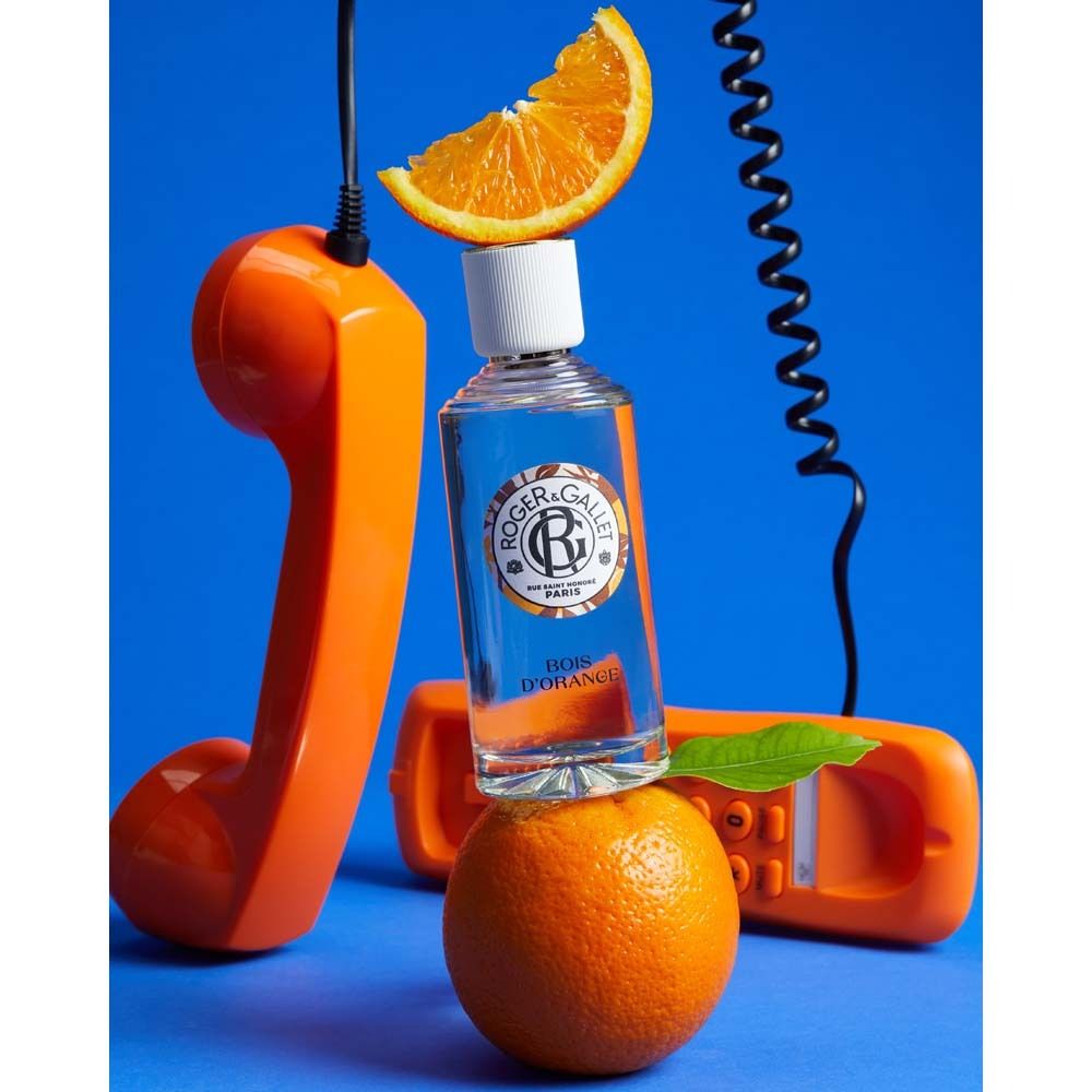 Flacone su arancia, circondato da telefoni e arancia. Logo e testo sull'etichetta. Scritta: Bois d'Orange.