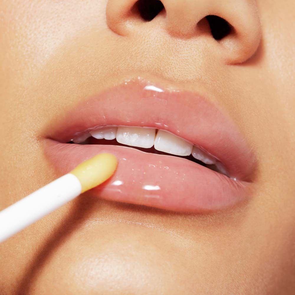 Labbra con olio labbra applicato. Applicatore visibile. Finitura lucida.