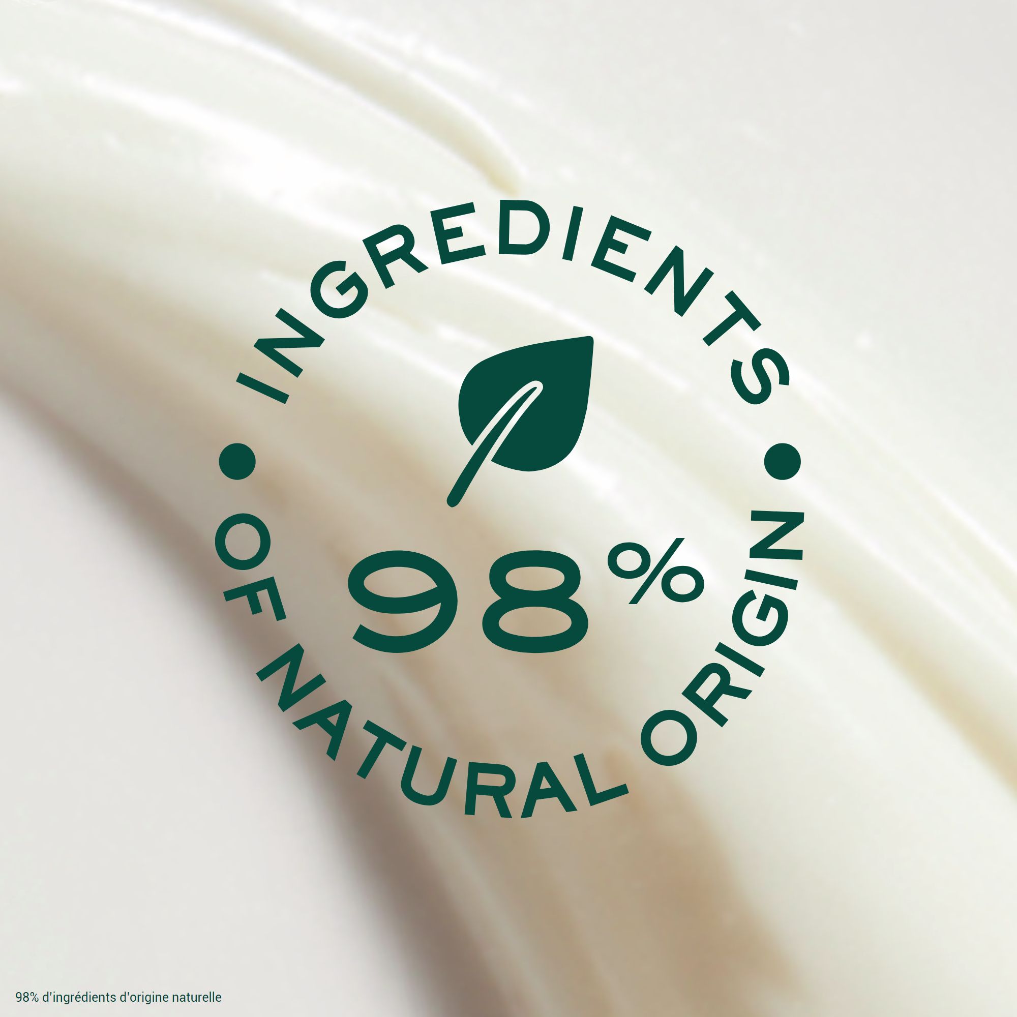 Macchia di crema bianca con logo foglia verde. Testo: 98% di ingredienti di origine naturale.
