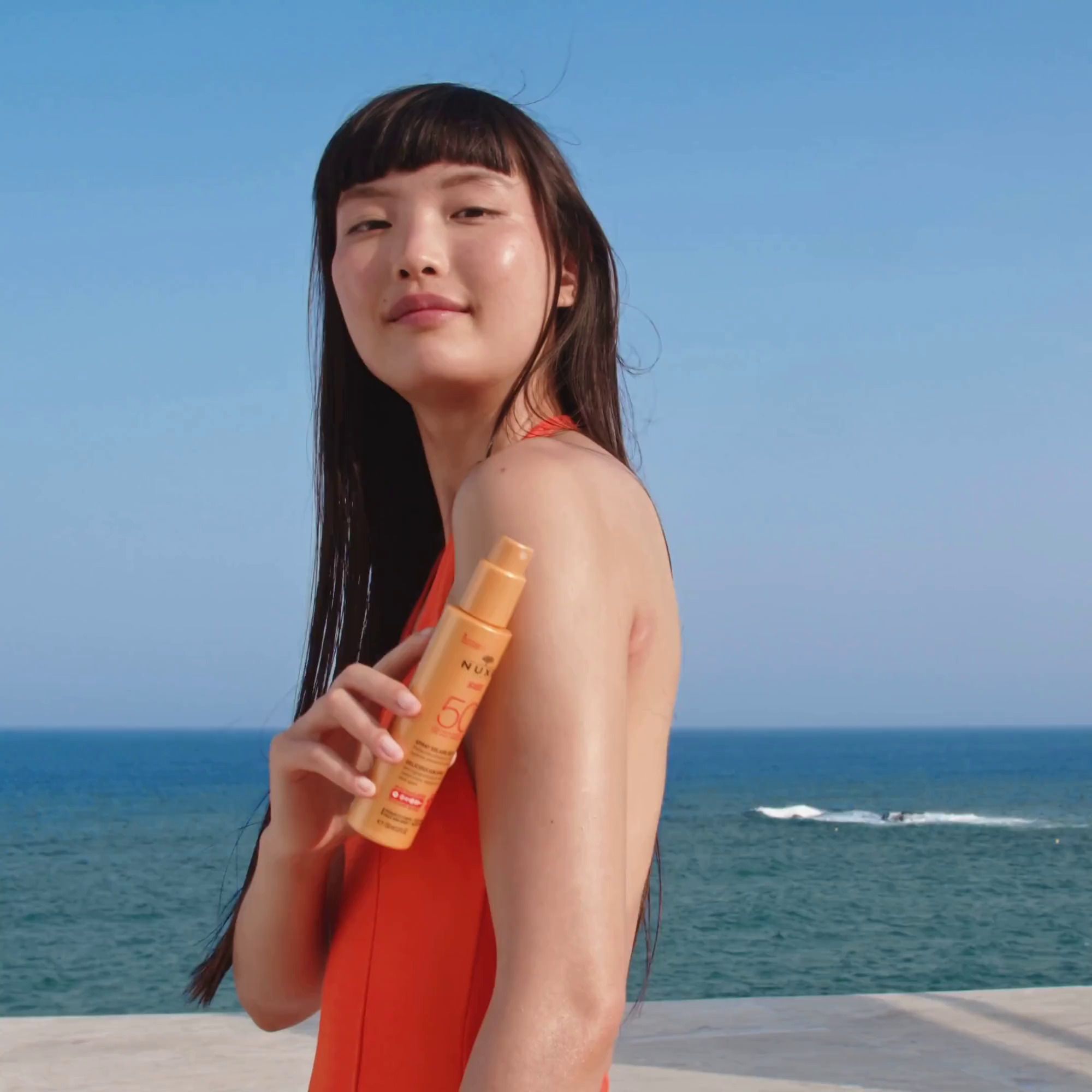 Donna tiene NUXE Sun in spiaggia. Mare sullo sfondo.