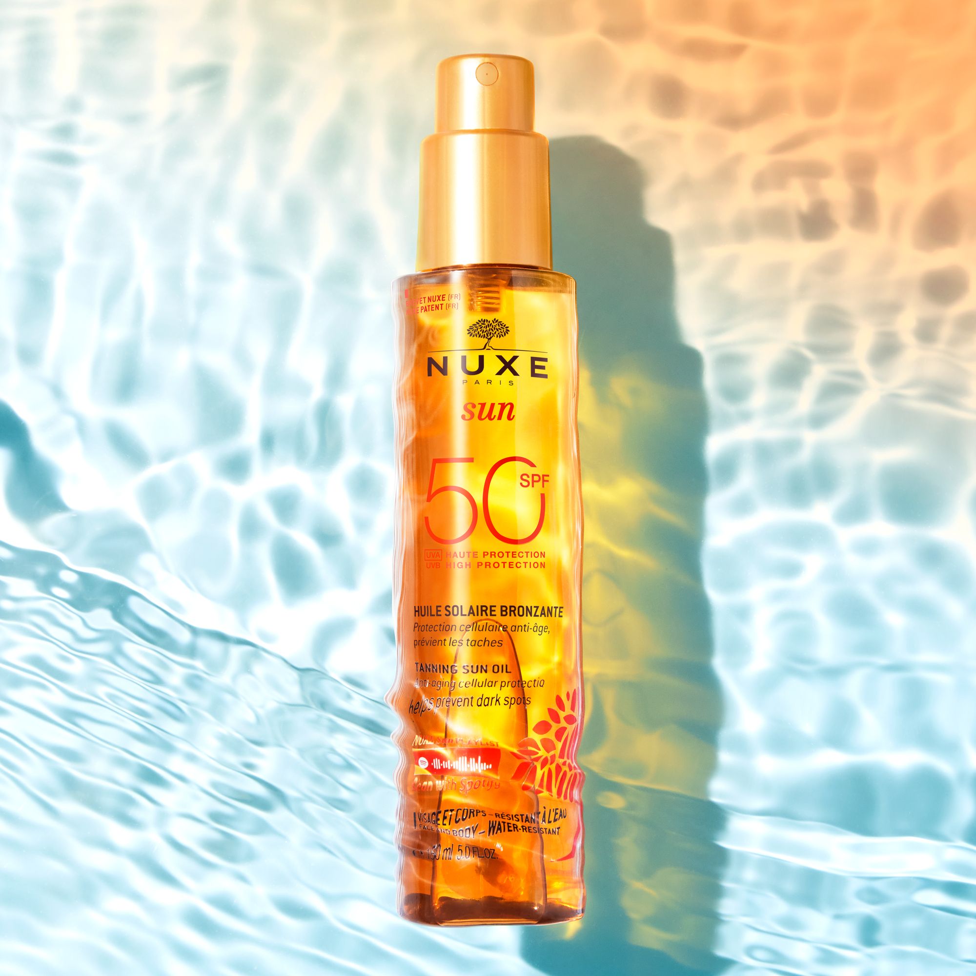 Flacone di olio solare Nuxe Sun su una superficie d'acqua con riflessi di luce.