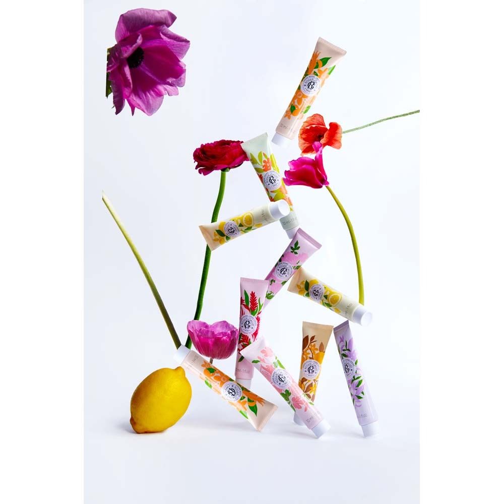 Diversi tubi di crema per le mani con motivi floreali, disposti con fiori e un limone su sfondo bianco.